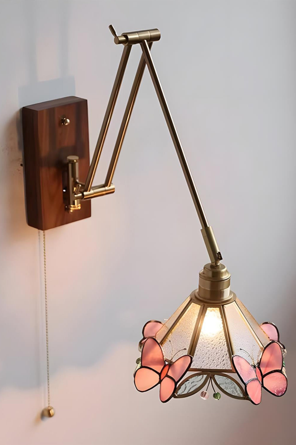 Cynthia Butterfly Articulated Wall Lamp | Stained Glass, Metal, Wood | Frontal angled view of the fully illuminated glass butterfly wall lamp casting a soft golden glow against a plain white wall | vexa lamps