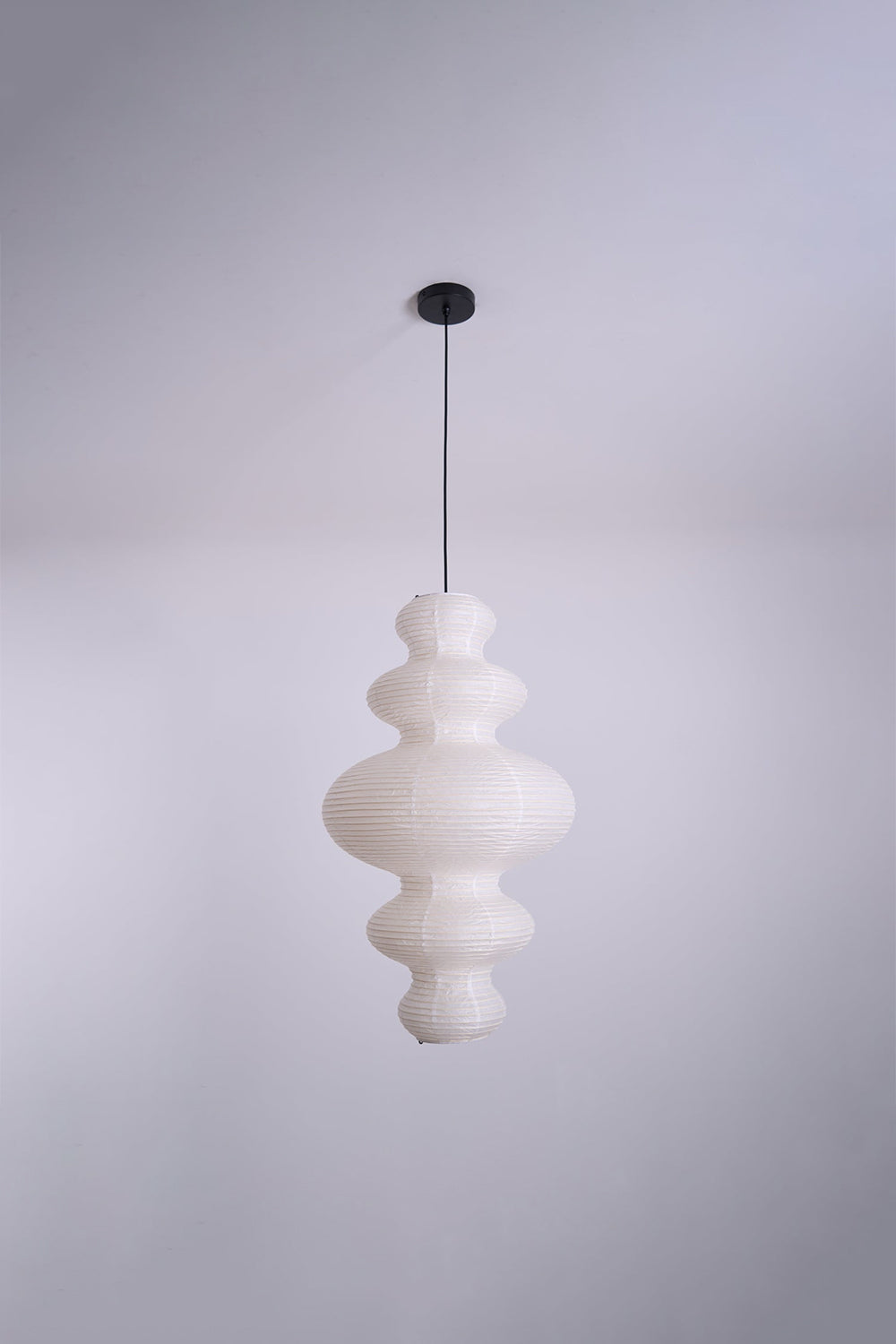 Isolde Stacked Paper Pendant Lamp | Textured Ribbed Paper | Full view of the sculptural light fixture hanging from a plain ceiling against a light wall | vexa lamps
