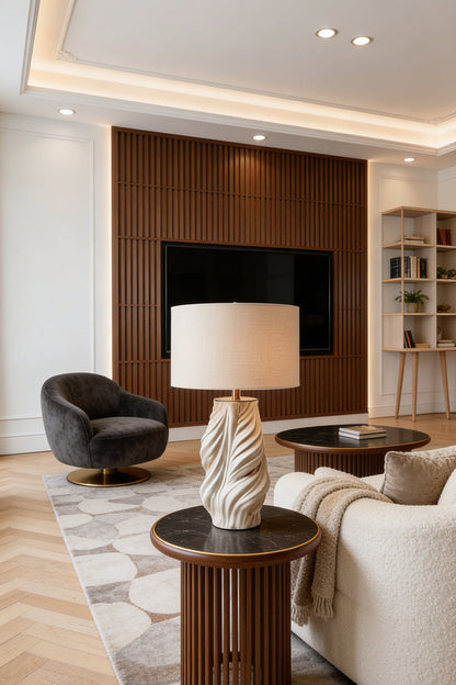 Adara Sculptural Ceramic Table Lamp | Ceramic, Fabric | Positioned on a round wooden end table next to a cream sofa in a contemporary living room with a dark wood media wall | vexa lamps