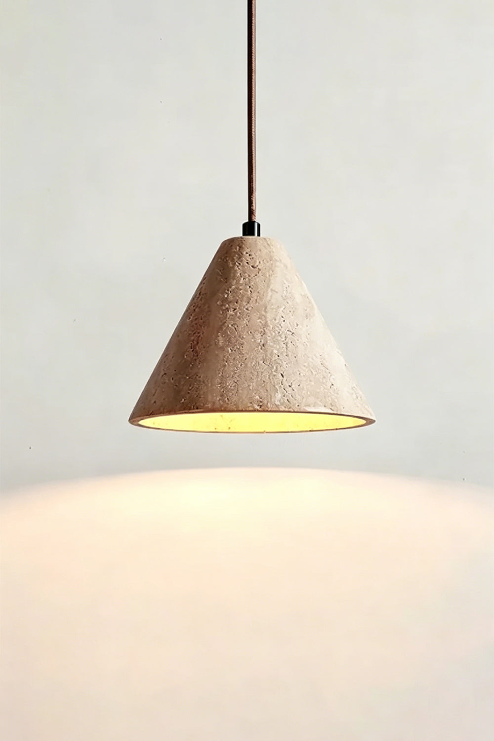 Lit Aethel Core Pendant Light | Beige Travertine, Metal | Wall view showing warm downward glow | vexa lamps