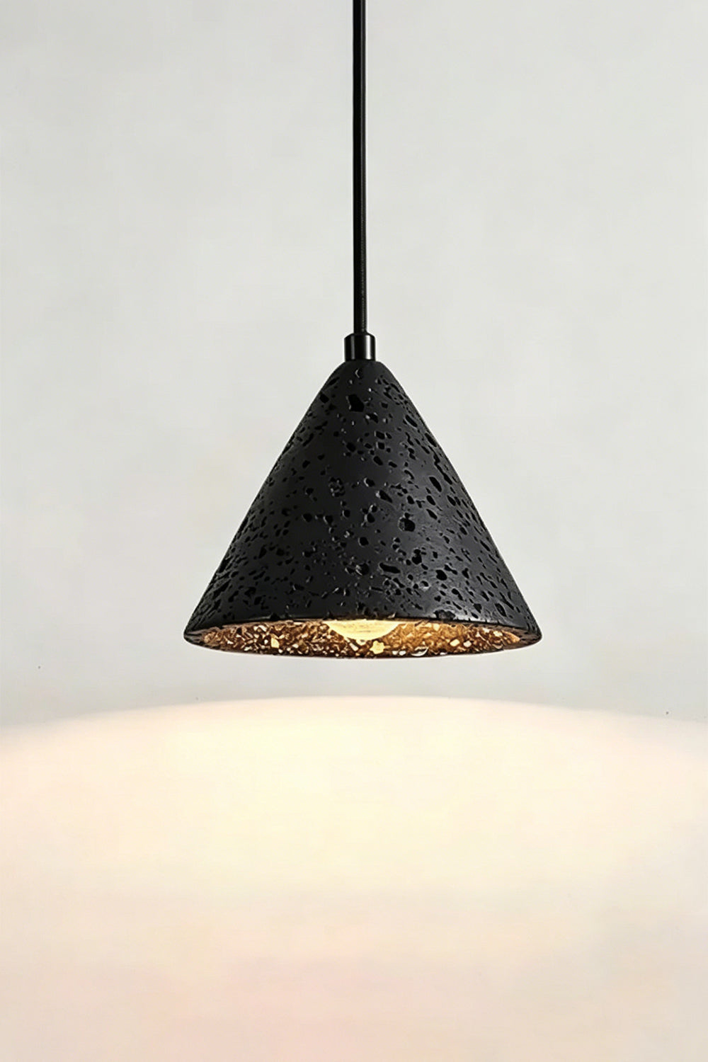 Lit Aethel Core Pendant Light | Black Travertine, Metal | Wall view showing textured stone and illumination | vexa lamps