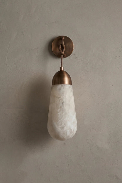 Alabaster Teardrop Wall Sconce featuring a teardrop alabaster shade with a metal backplate on a textured wall.