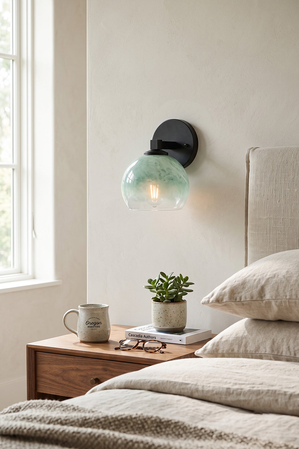 Alba Ombre Glass Wall Sconce illuminating a bedside table with a plant and mug, showcasing hand-blown glass design.
