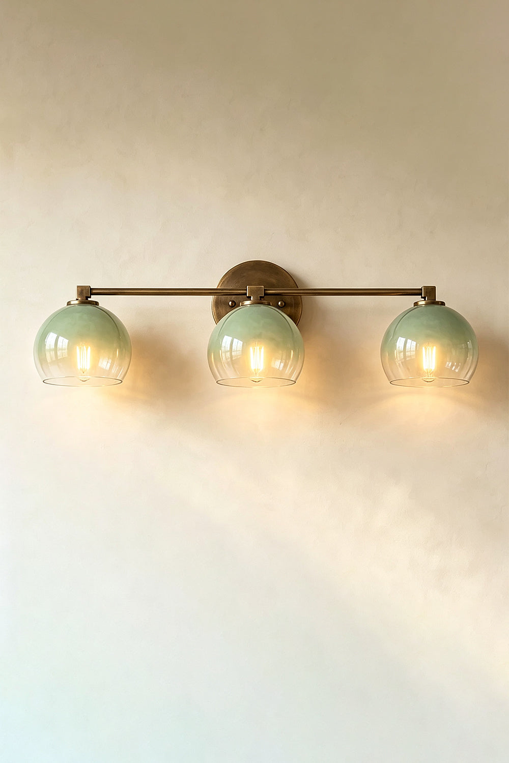 Alba Ombre Glass Wall Sconce featuring three hand-blown glass globes with a green to clear gradient on a bronze bar.