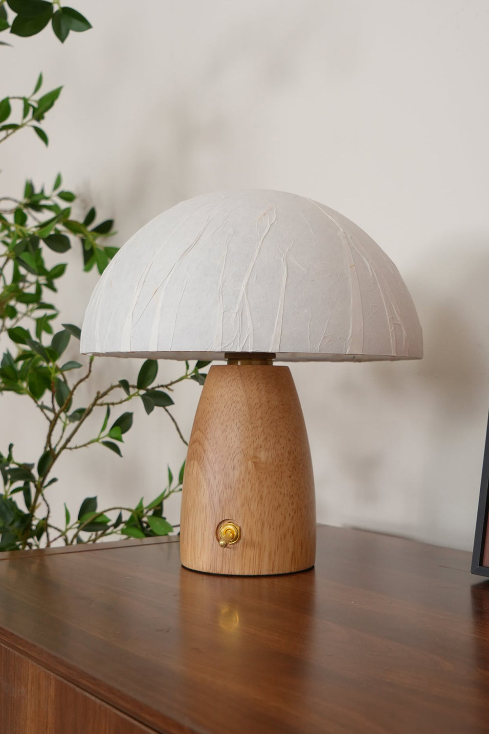 Alice Mushroom Table Lamp | Wood, Glass | Close-up shot of the lit mushroom lamp on a rich dark wood desk next to climbing green plant vines | vexa lamps