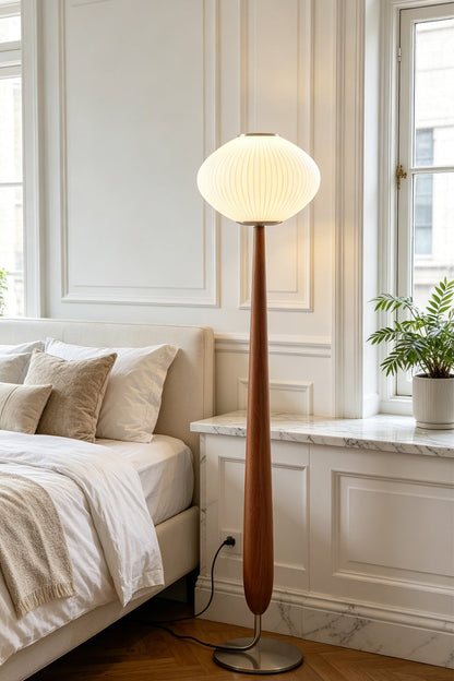 Arden Walnut Floor Lamp | Wood, Metal, Fabric | Providing soft bedtime ambient illumination in a cozy bedroom corner next to a cream platform bed and white paneled walls | vexa lamps