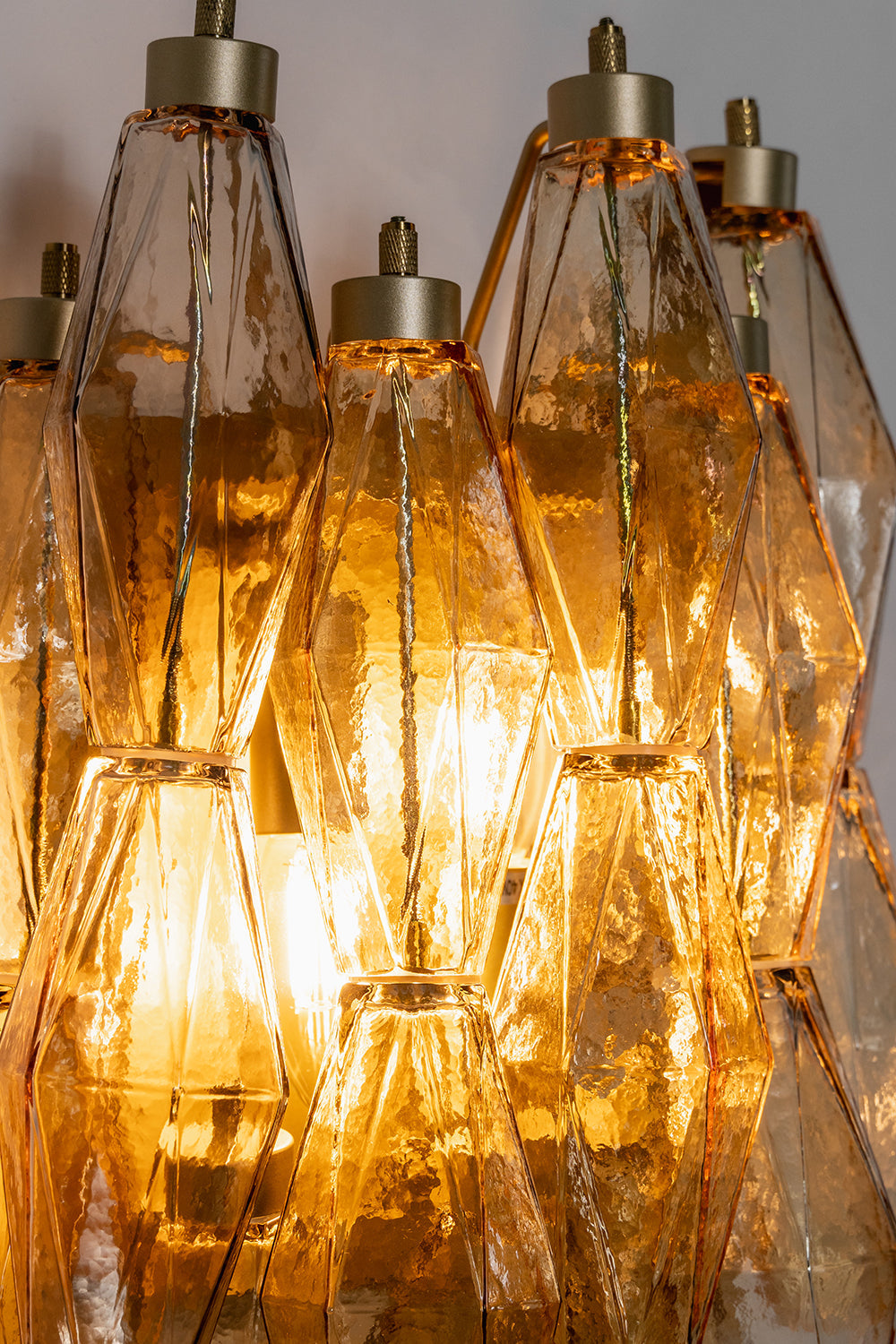 Close-up of lit amber polyhedral glass | Metal, Glass | Detail view of the warm glow and multifaceted glass prisms | vexa lamps
