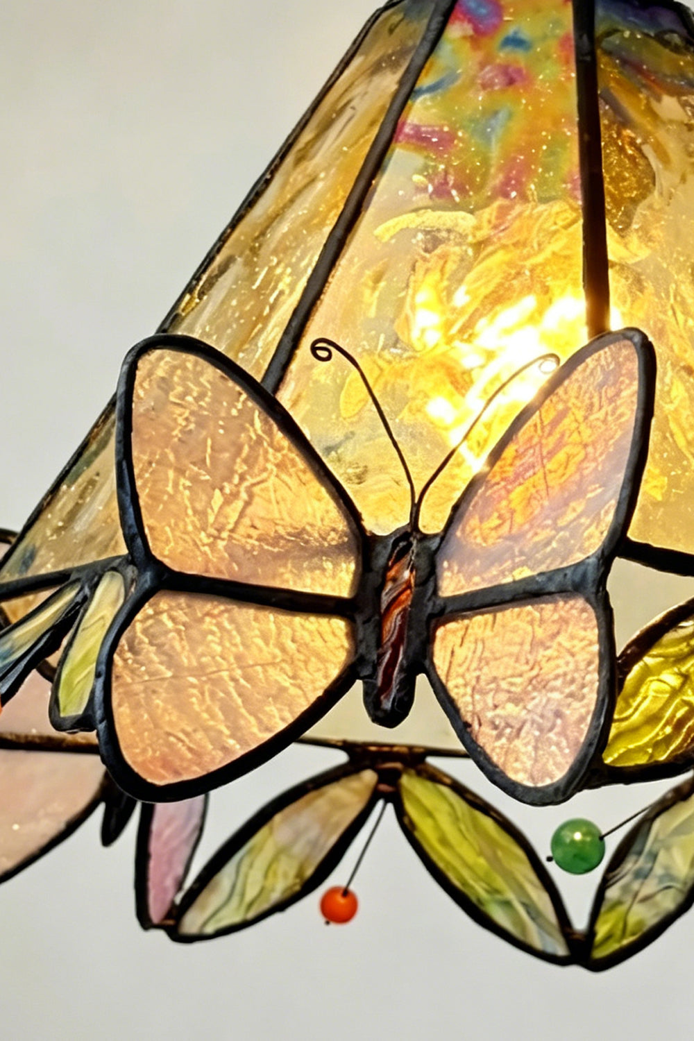 Aura Vine Stained Glass Wall Sconce | Glass, Metal | Macro focus on the illuminated yellow glass pattern, a butterfly motif, and colorful small glass gems along the scalloped rim | Detail shot | vexa lamps