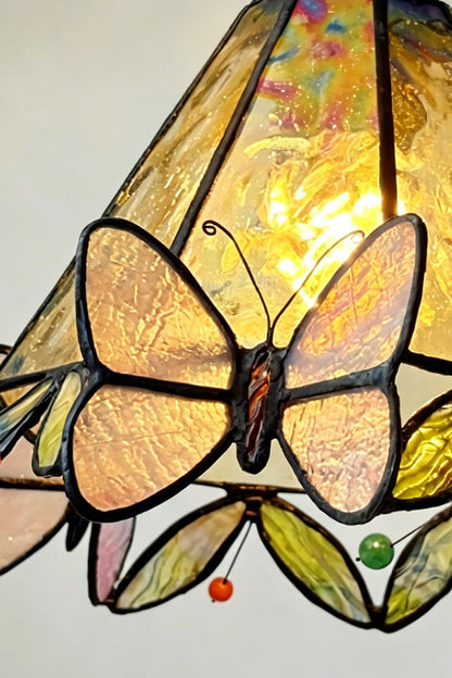 Aura Vine Stained Glass Wall Sconce | Glass, Metal | Macro focus on the illuminated yellow glass pattern, a butterfly motif, and colorful small glass gems along the scalloped rim | Detail shot | vexa lamps