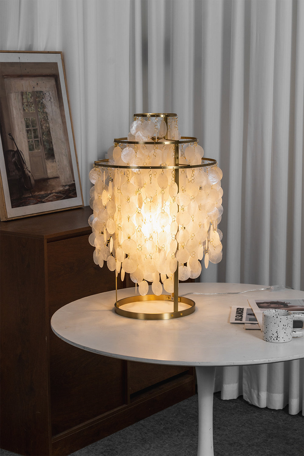 Aurelia Tiered Capiz Table Lamp | Capiz Shell, Metal | Lit on a modern white round table next to sheer white curtains in a minimalist room | vexa lamps