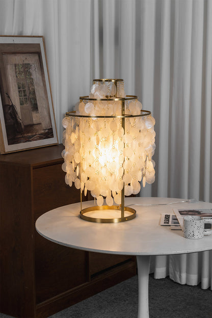 Aurelia Tiered Capiz Table Lamp | Capiz Shell, Metal | Lit on a modern white round table next to sheer white curtains in a minimalist room | vexa lamps