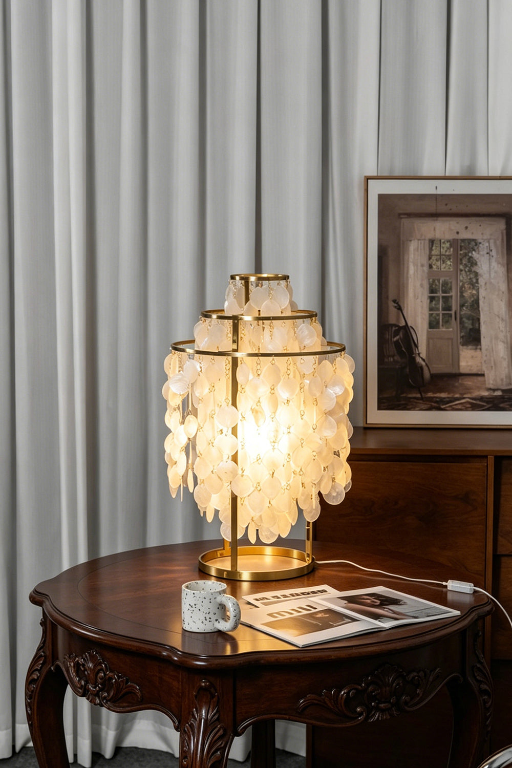 Aurelia Tiered Capiz Table Lamp | Capiz Shell, Metal | Placed on a round antique wooden table, casting a warm ambient light in a cozy dining space | vexa lamps