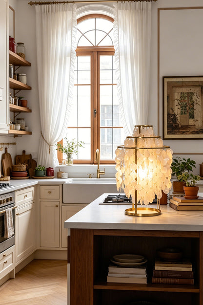 Aurelia Tiered Capiz Table Lamp | Capiz Shell, Metal | Set on a white marble kitchen island counter providing a warm inviting glow next to modern cabinetry | vexa lamps