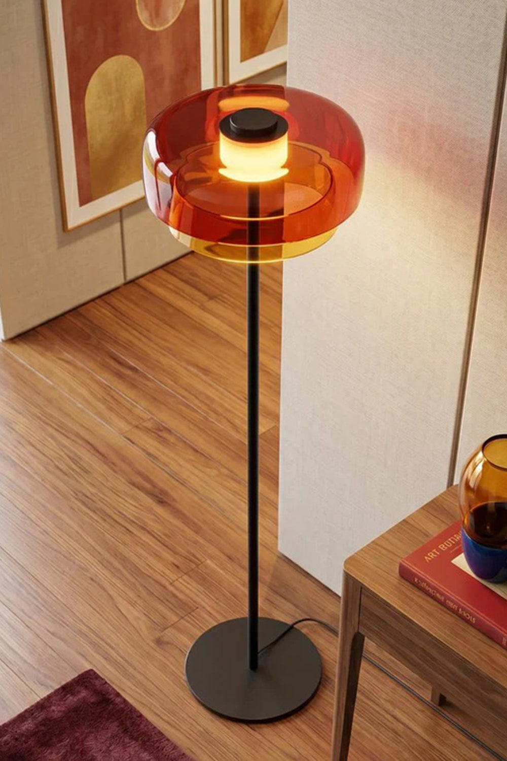 Aven Minimalist Architectural Floor Lamp | Glass, Metal | Elevated angled close-up view of the glowing orange glass variant standing elegantly on a dark wood parquet floor | Detail shot | vexa lamps