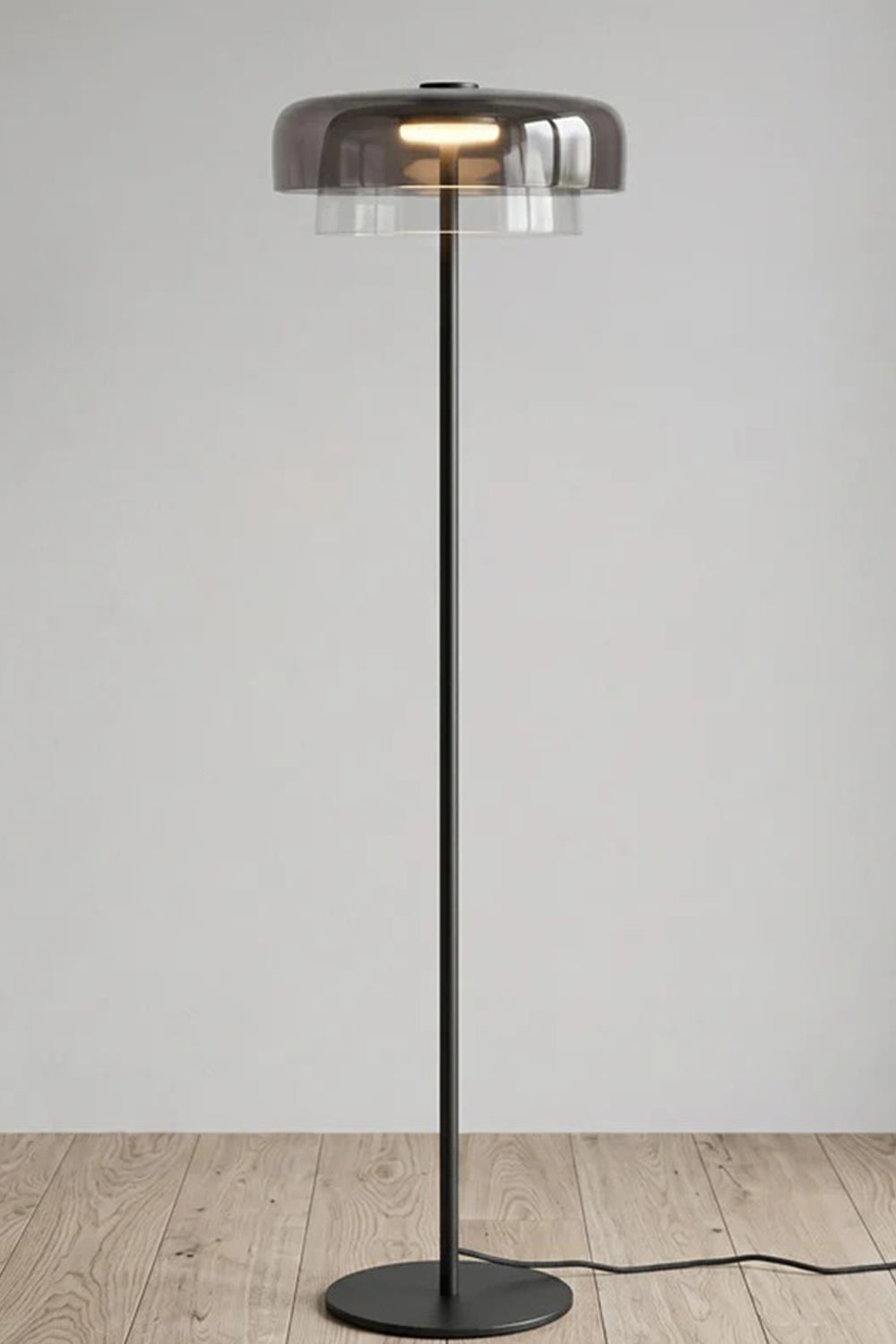 Aven Minimalist Architectural Floor Lamp | Glass, Metal | Studio front view of the fully illuminated smoky grey glass floor lamp variant displayed on a clean wooden floor | vexa lamps