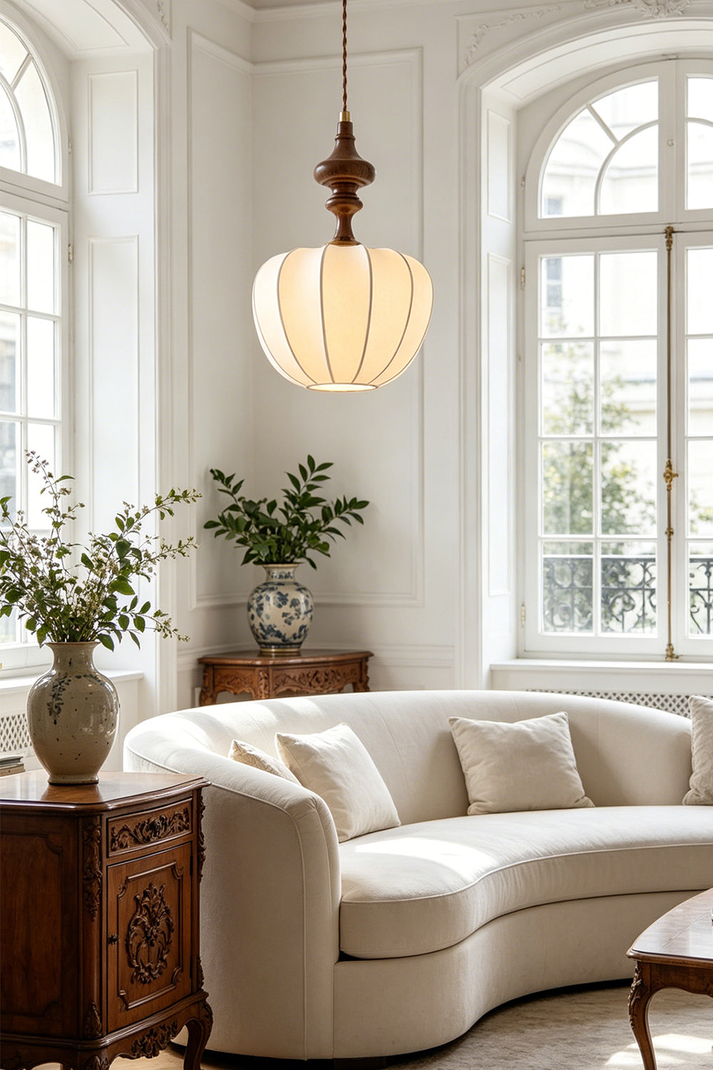 Baird Mid-Century Silk Pendant Light illuminating a stylish living room with a curved sofa and decorative plants.
