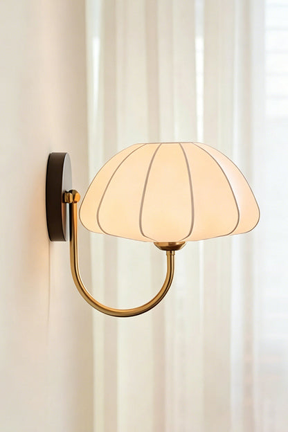 Baird Mid Century Pumpkin Wall Lamp | Metal, Fabric, Wood | Side profile view of the illuminated wall lamp next to soft white sheer curtains | vexa lamps
