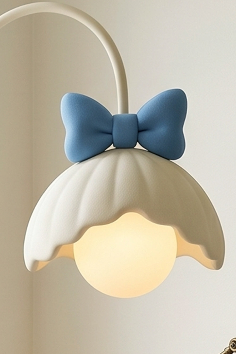 Bella Bow Arched Floor Lamp | Metal, Resin | Close-up view of the lit blue bow variant radiating a soft warm light from beneath its white flower-shaped shade | Detail shot | vexa lamps