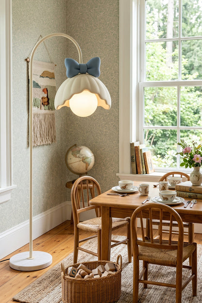 Bella Bow Arched Floor Lamp | Metal, Resin | Blue bow version casting a warm glow over a wooden child's activity table and chair set in a sunlit playroom | vexa lamps