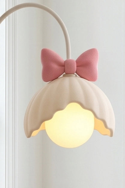 Bella Bow Arched Floor Lamp | Metal, Resin | Close-up side profile of the lit pink bow variant showcasing the glowing round glass globe bulb under the scalloped shade | Detail shot | vexa lamps