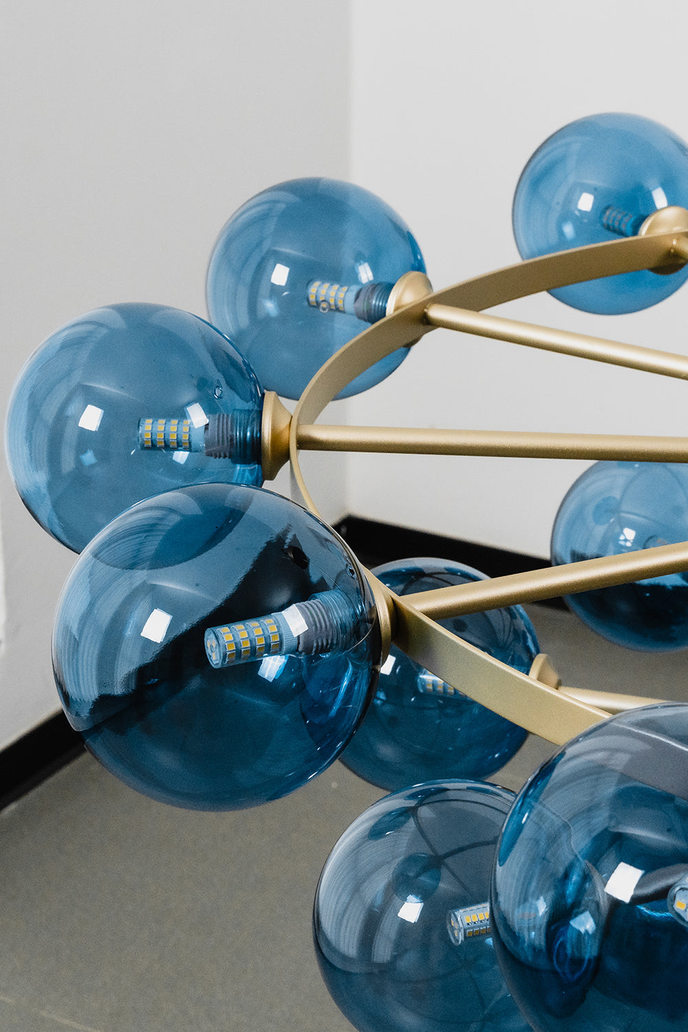 Blue Glass Bubble Globe Tiered Chandelier | Blue Glass and Brass Metal | Close-up side perspective focusing on a cluster of blue bubble globes and brass rods | vexa lamps