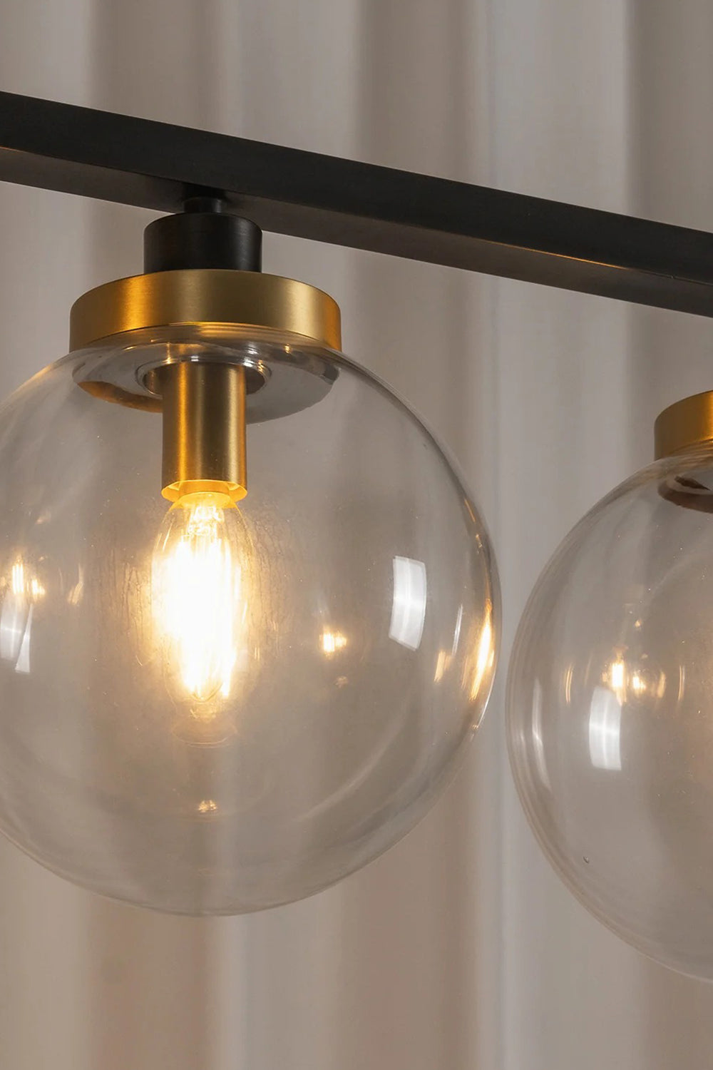Brooks Linear Glass Globe Chandelier | Glass, Metal | Macro close-up view of a fully illuminated clear glass globe sphere highlighting the warm glowing bulb filament and gold brass cap | Detail shot | vexa lamps