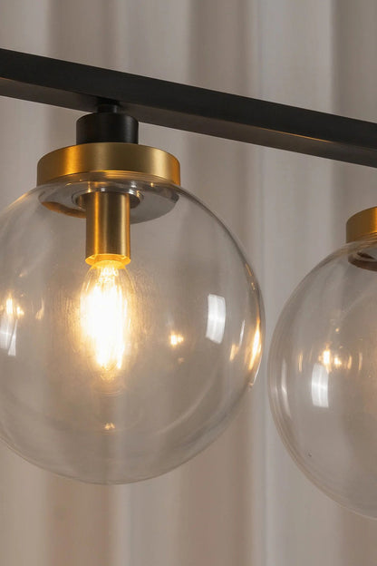 Brooks Linear Glass Globe Chandelier | Glass, Metal | Macro close-up view of a fully illuminated clear glass globe sphere highlighting the warm glowing bulb filament and gold brass cap | Detail shot | vexa lamps