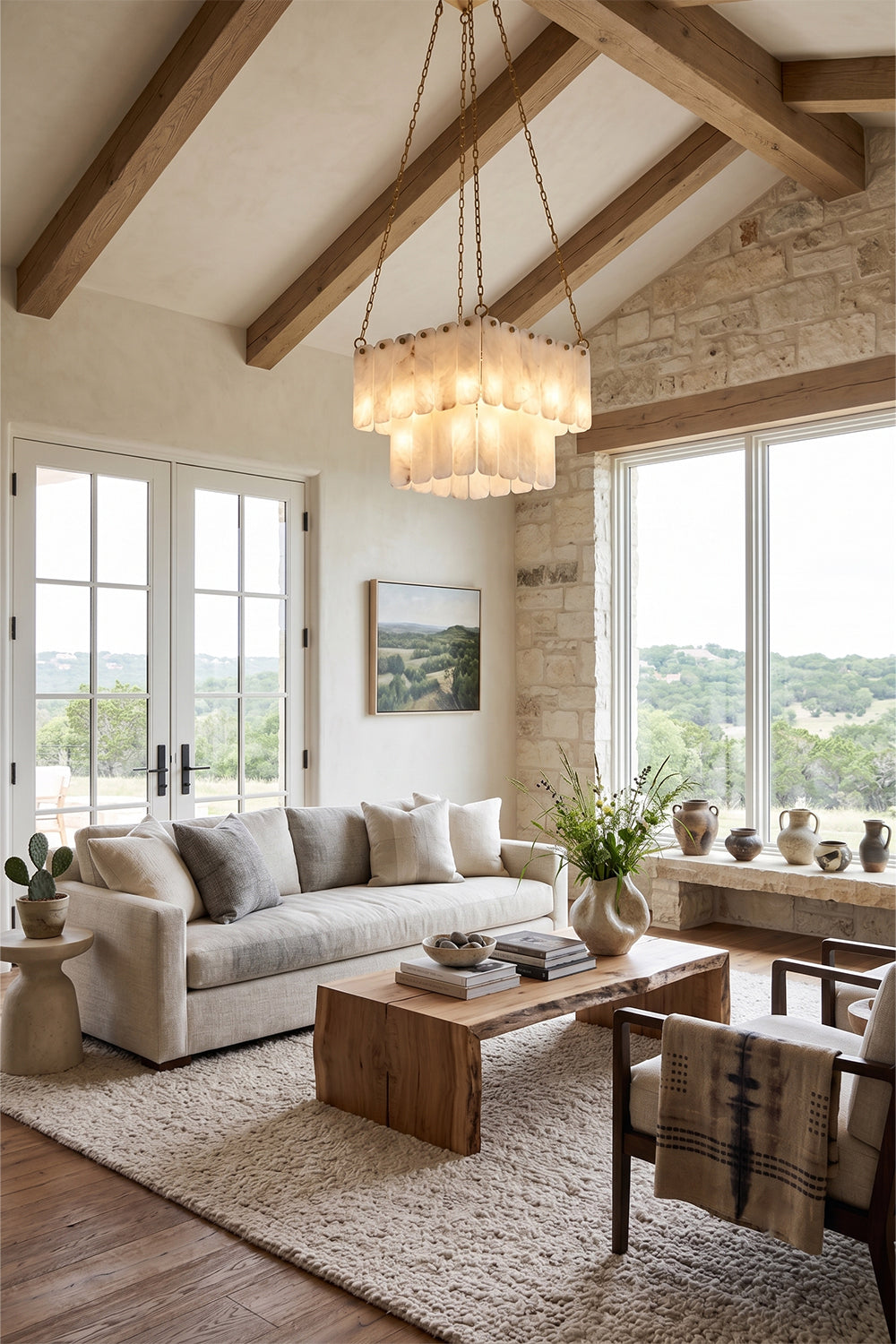 Callista Tiered Alabaster Chandelier | Alabaster, Metal | Hanging as a grand centerpiece in a rustic modern living room with high vaulted ceilings, exposed wooden beams, and a cream fabric sofa | vexa lamps