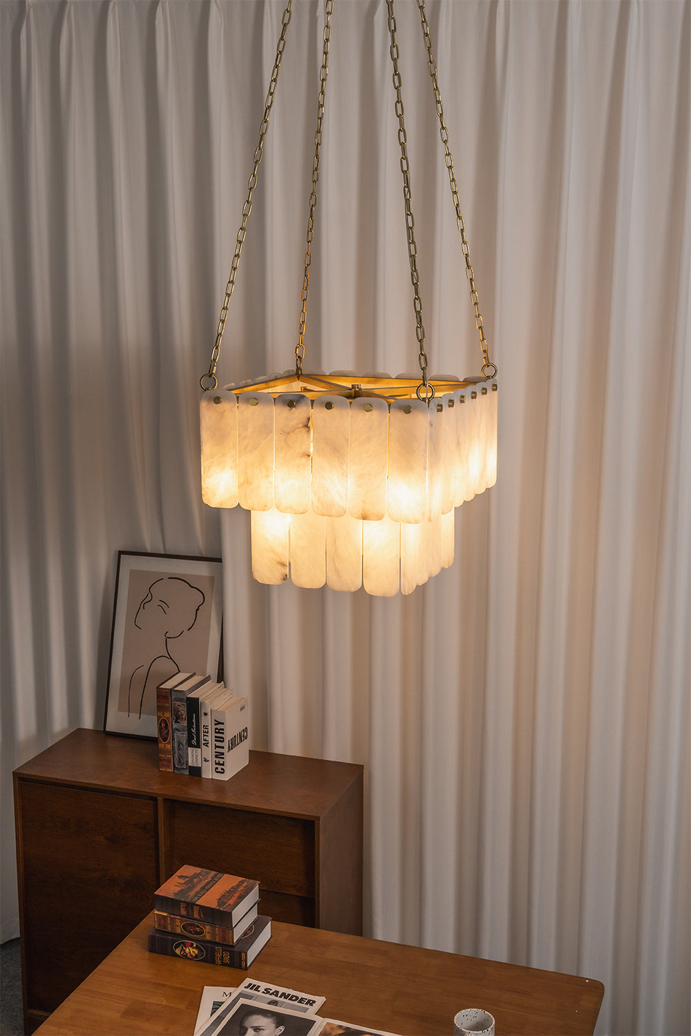 Callista Tiered Alabaster Chandelier | Alabaster, Metal | Staged in a contemporary interior corner, casting a cozy golden ambient glow near vertically pleated curtains and a wooden chest | vexa lamps