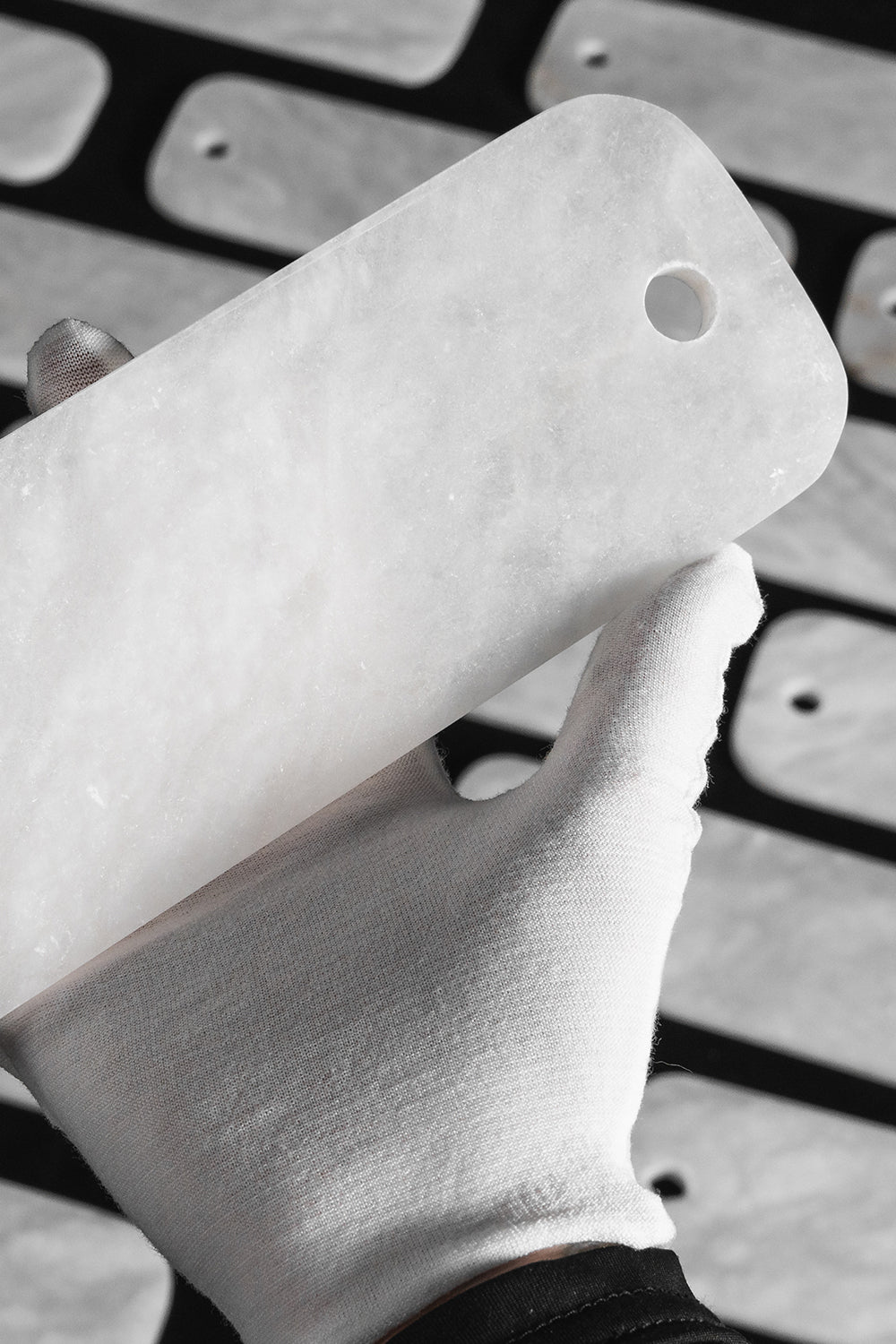 Callista Tiered Alabaster Chandelier | Alabaster, Metal | A gloved hand holding up a single polished rectangular white alabaster stone component to demonstrate its opacity and fine texture | Detail shot | vexa lamps