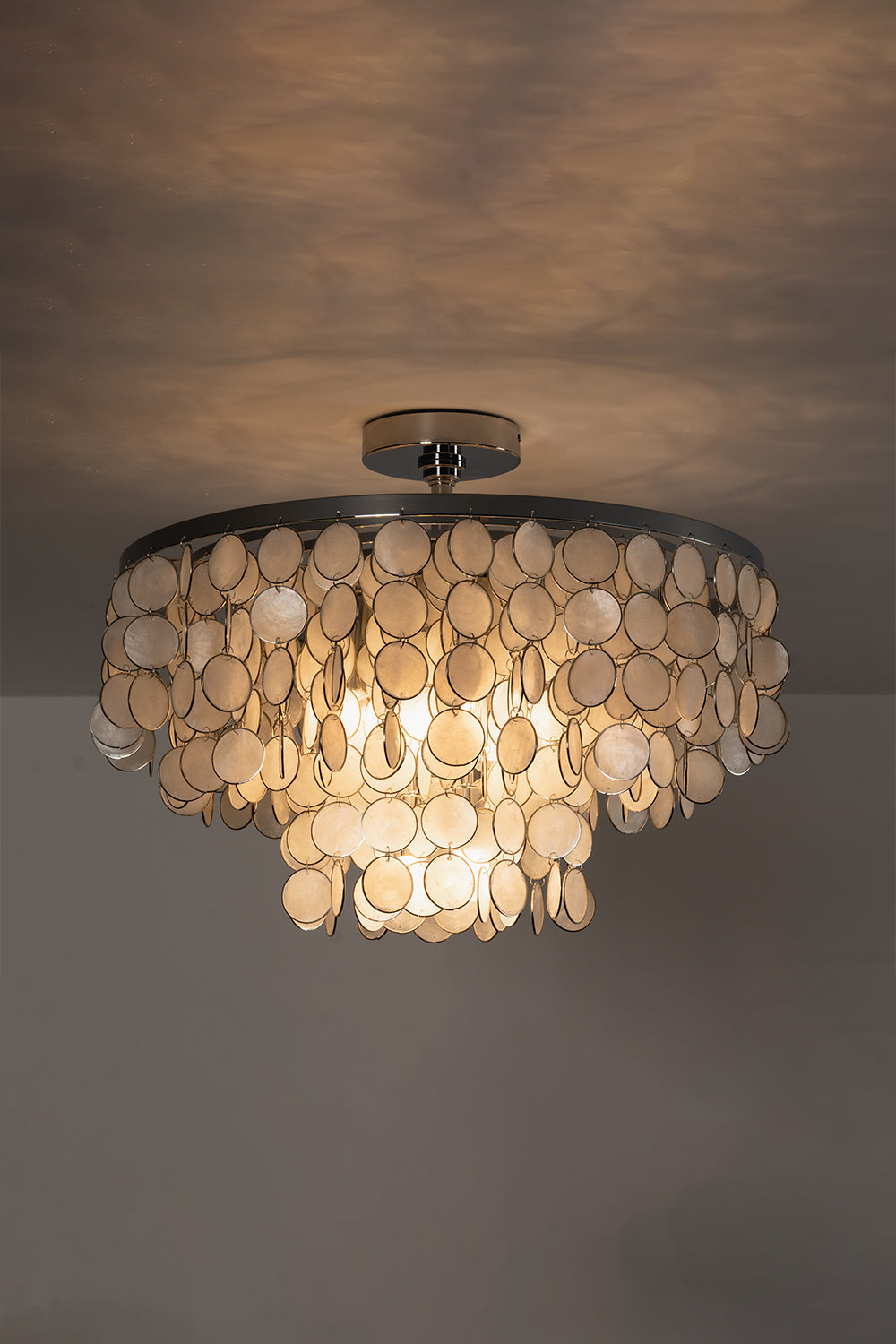 Lit Capiz shell ceiling light against ceiling | Shell | Iron | Low-light mood shot showing warm glow on textures | vexa lamps