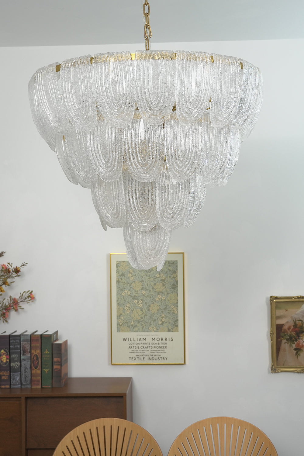 Lit tiered glass petal chandelier against white wall | Metal, Glass | Centered view showing the warm glowing texture | vexa lamps