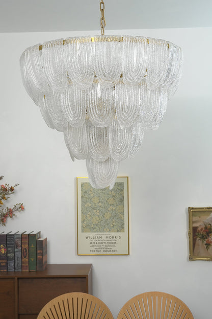 Lit tiered glass petal chandelier against white wall | Metal, Glass | Centered view showing the warm glowing texture | vexa lamps