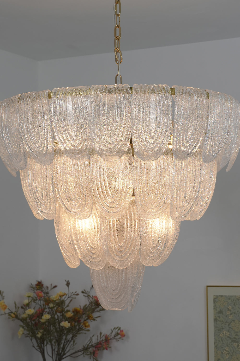 Lit cascading glass chandelier against neutral wall | Metal, Glass | Side perspective showing the tiered petal arrangement | vexa lamps
