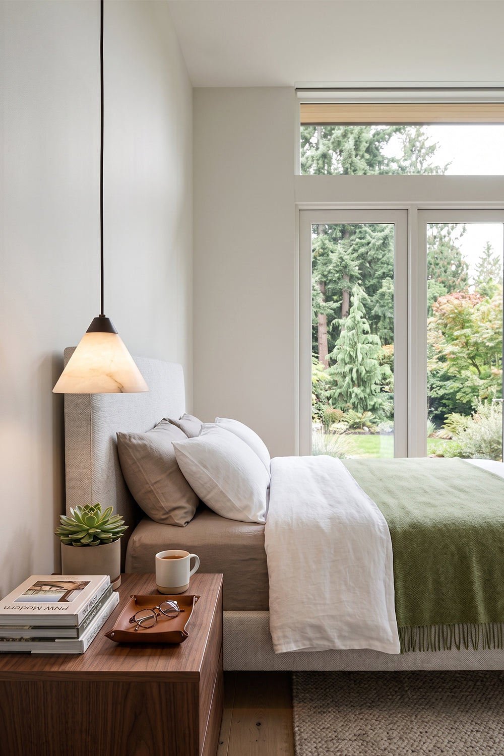 Caspian Conical Alabaster Pendant Light | Natural Alabaster and Brass | Suspended above a wooden nightstand in a cozy bedroom with neat green and white linens | vexa lamps