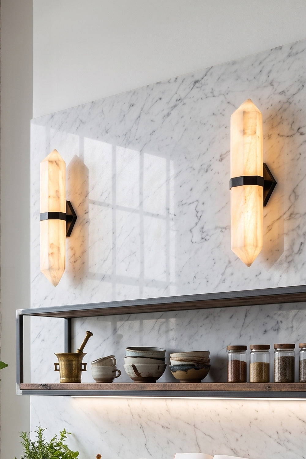 Cassian Faceted Alabaster Wall Sconce illuminating a modern kitchen with marble walls and open shelving.