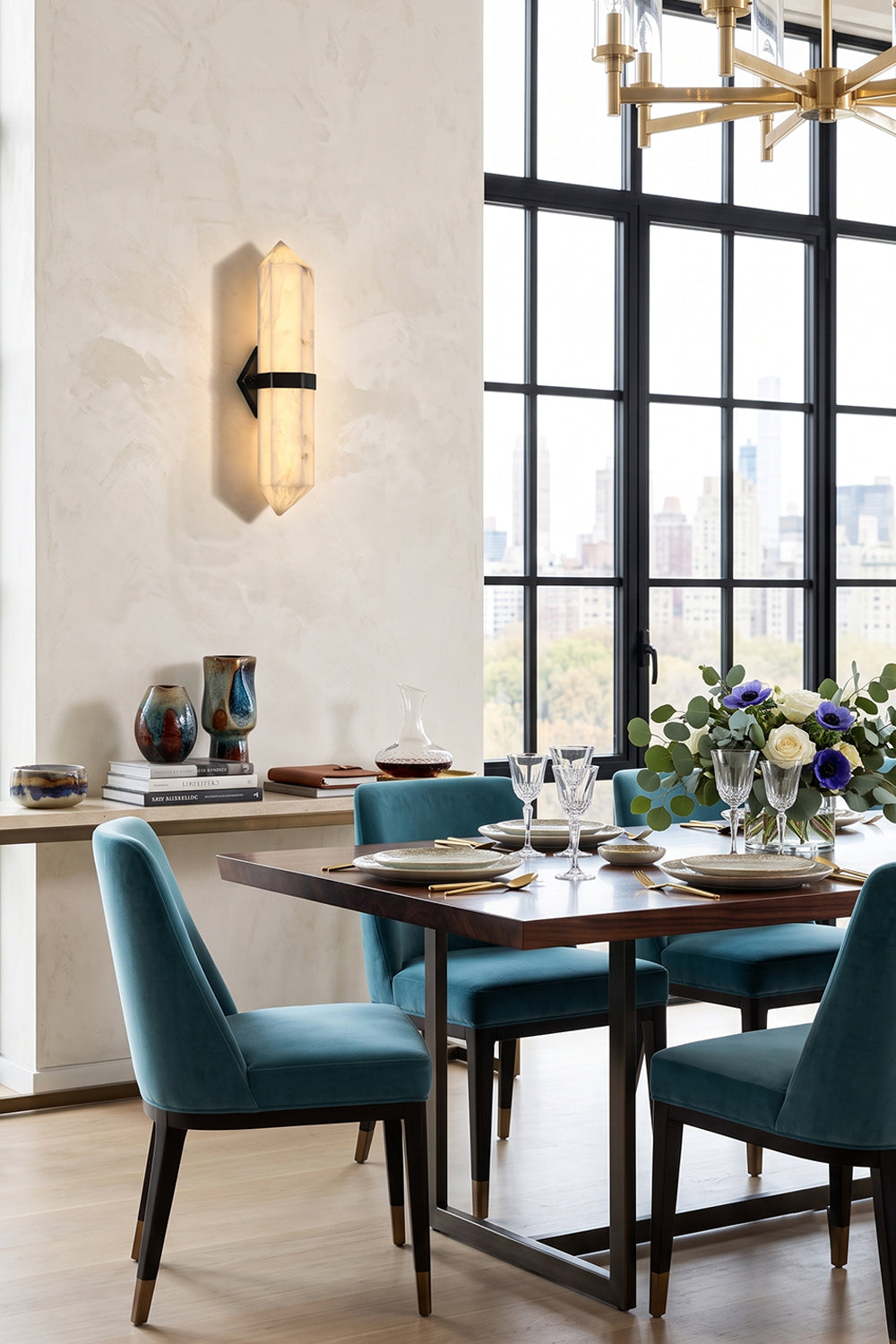 Cassian Faceted Alabaster Wall Sconce illuminating a dining area with modern furniture and a scenic view.
