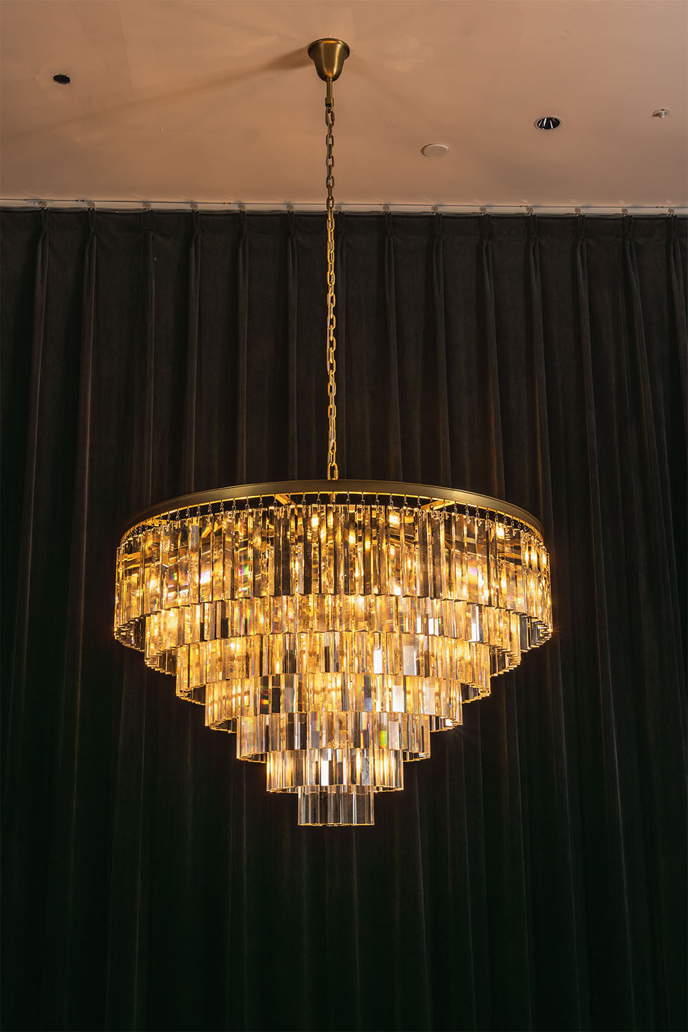 Cassian Tiered Prism Ring Chandelier | Clear Prism Glass and Brass | Full illuminated view displayed against a dark green curtain backdrop | vexa lamps