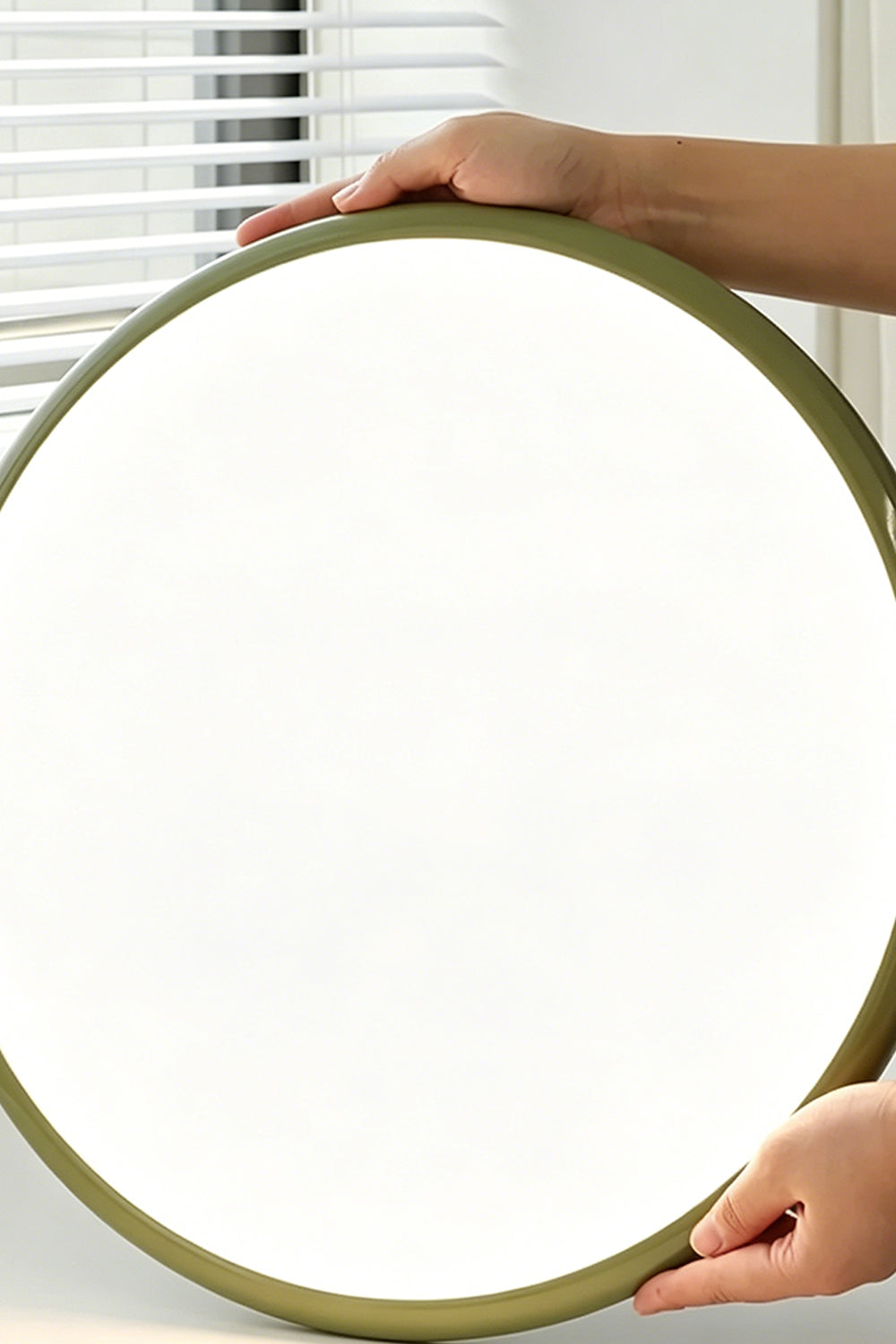 Celestial Disc Lacquered Ceiling Light | Acrylic, Metal | A person's hands holding the unlit green-trimmed circular light, demonstrating its large scale against a grey wall | Scale reference shot | vexa lampsCelestial Disc