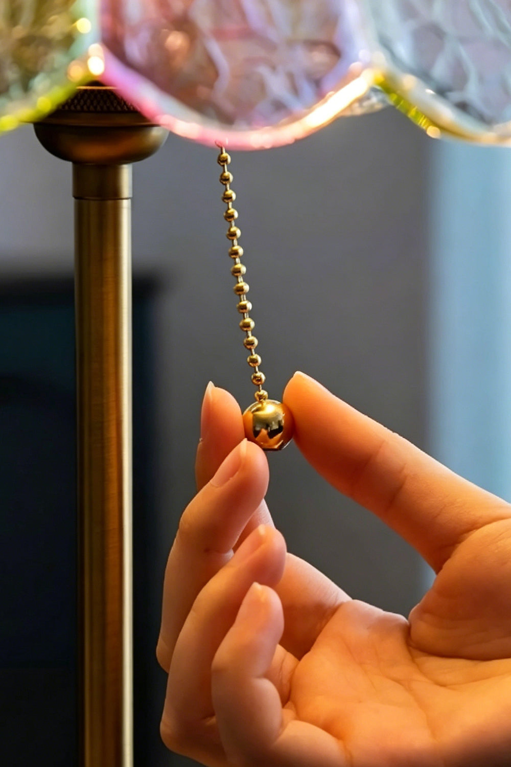 Clara Vintage Pastel Glass Table Lamp | Glass, Metal | A close-up view of a hand pulling the vintage gold ball chain switch beneath the glowing shade | Detail shot | vexa lamps