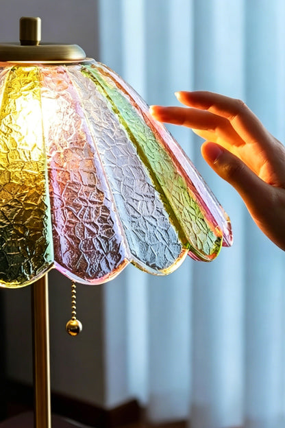 Clara Vintage Pastel Glass Table Lamp | Glass, Metal | A hand gently touching the scalloped edge of the fully illuminated colorful glass lampshade near a window | vexa lamps