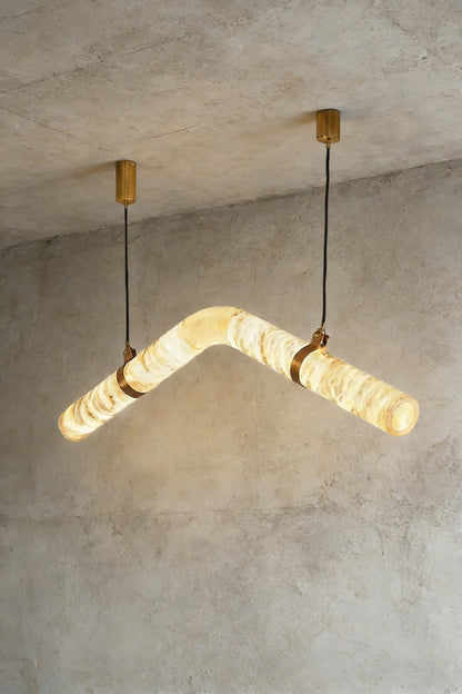 Lit undulating alabaster tube chandelier against grey ceiling | Alabaster, Brass | Side perspective showing the organic shape | vexa lamps