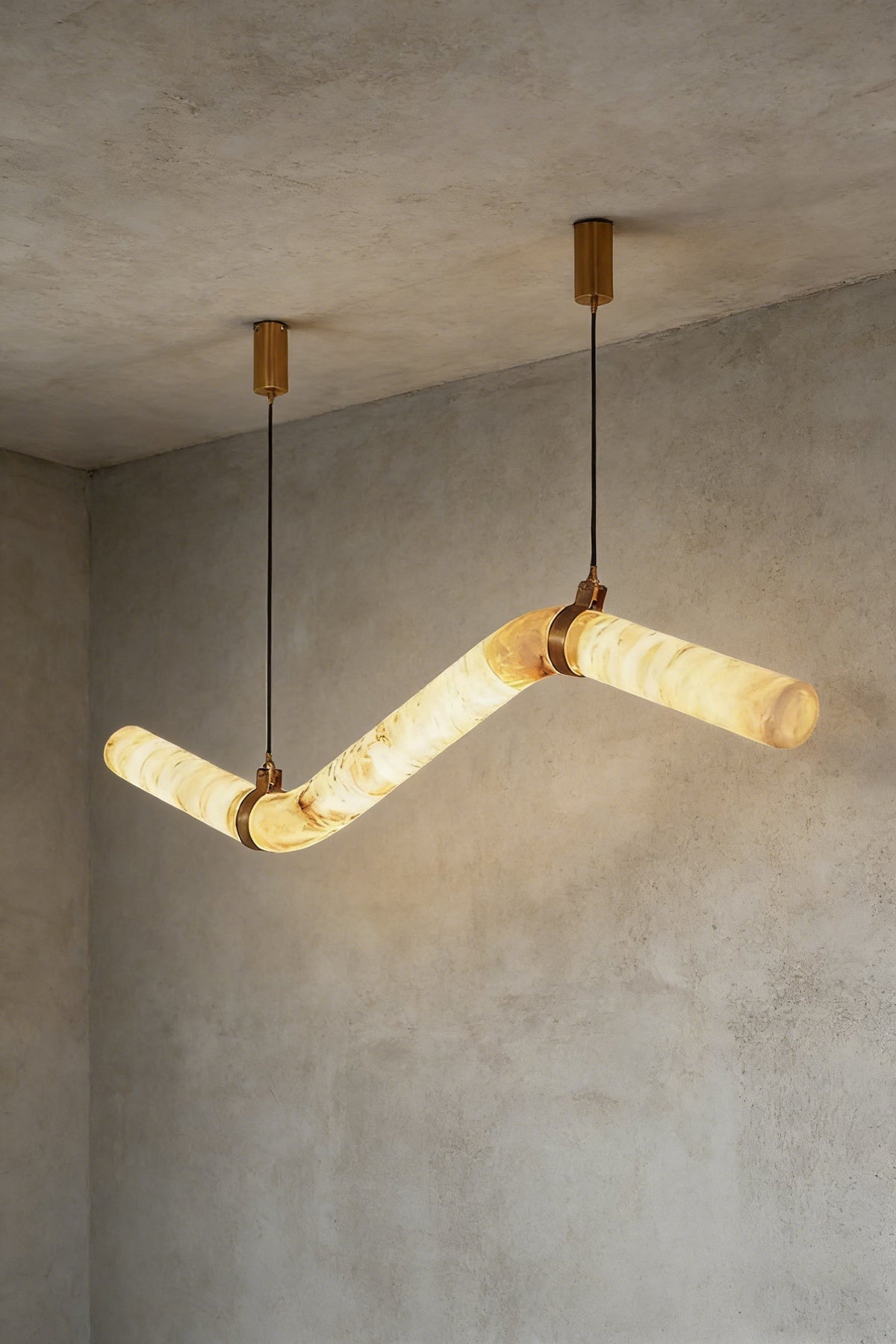 Lit undulating alabaster tube chandelier against grey ceiling | Alabaster, Brass | Side perspective showing the organic shape | vexa lamps