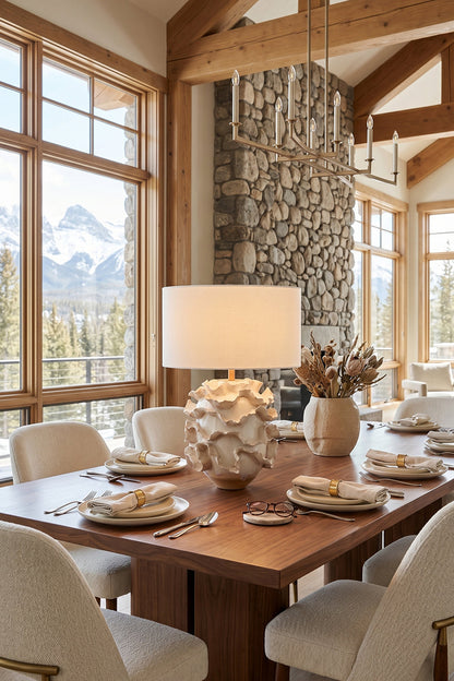 Coralia Ruffled Ceramic Table Lamp placed on a wooden dining table, with elegant plates and a scenic mountain view.