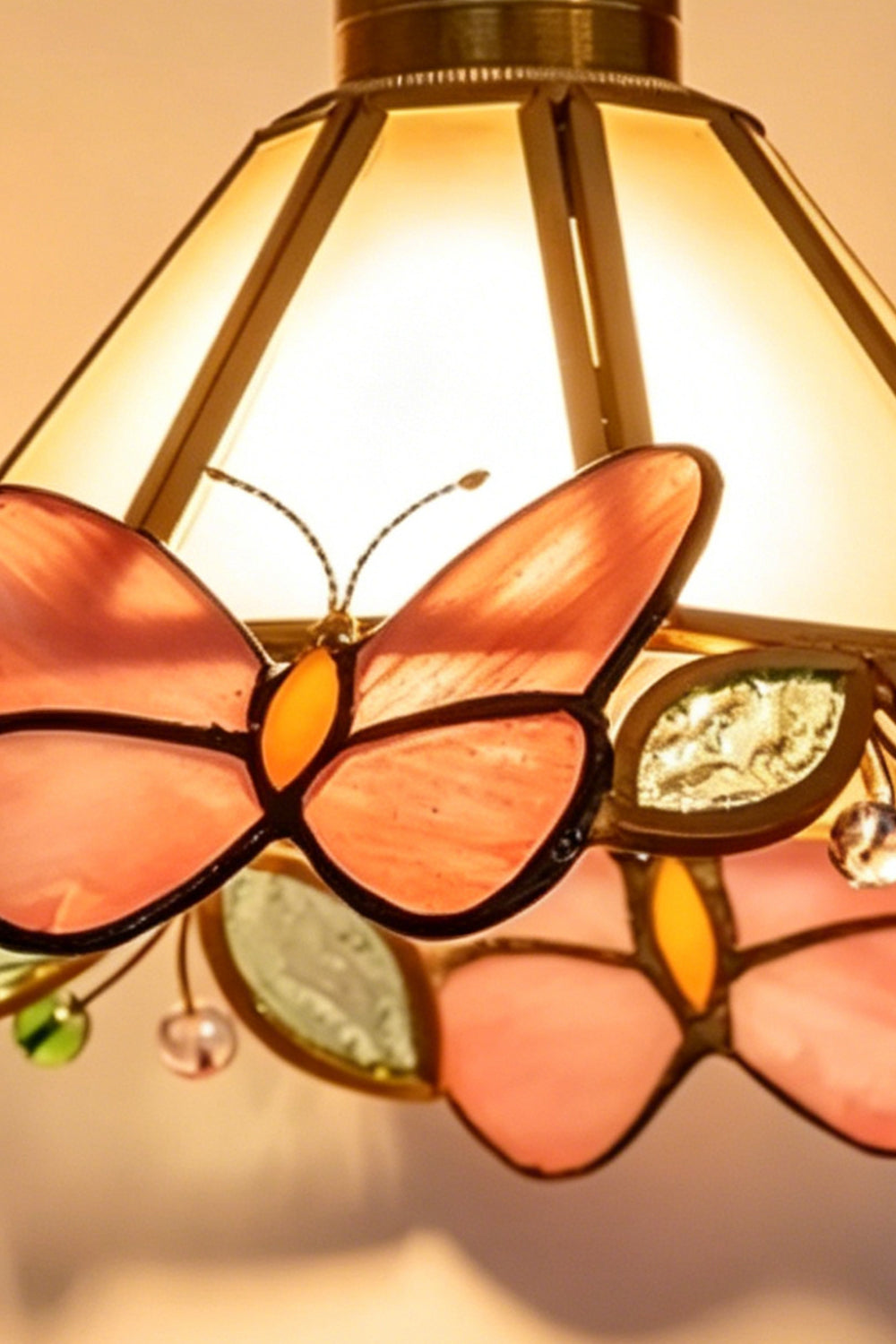 Cynthia Butterfly Articulated Wall Lamp | Stained Glass, Metal, Wood | Close-up view of the fully illuminated stained glass lampshade highlighting the vibrant pink and orange butterflies under warm light | Detail shot | vexa lamps