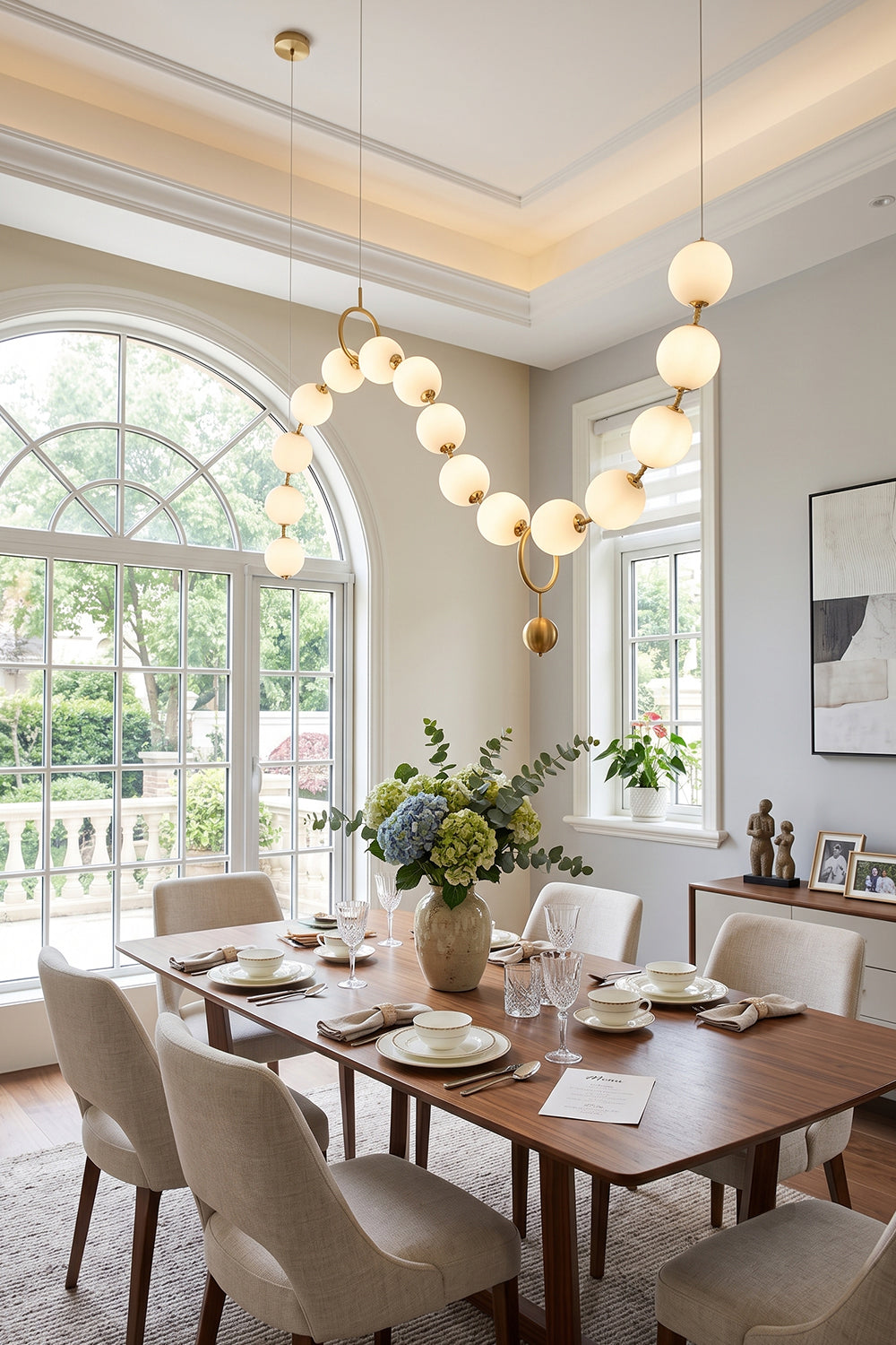 Delphine Pearl Strand Chandelier elegantly illuminating a dining room with a wooden table and floral centerpiece.