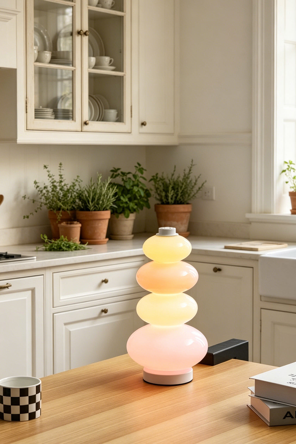 Dolce Stacked Pastel Glass Table Lamp | Glass, Metal | Standing as a playful accent on a warm wooden kitchen island table surrounded by potted green plants | vexa lamps