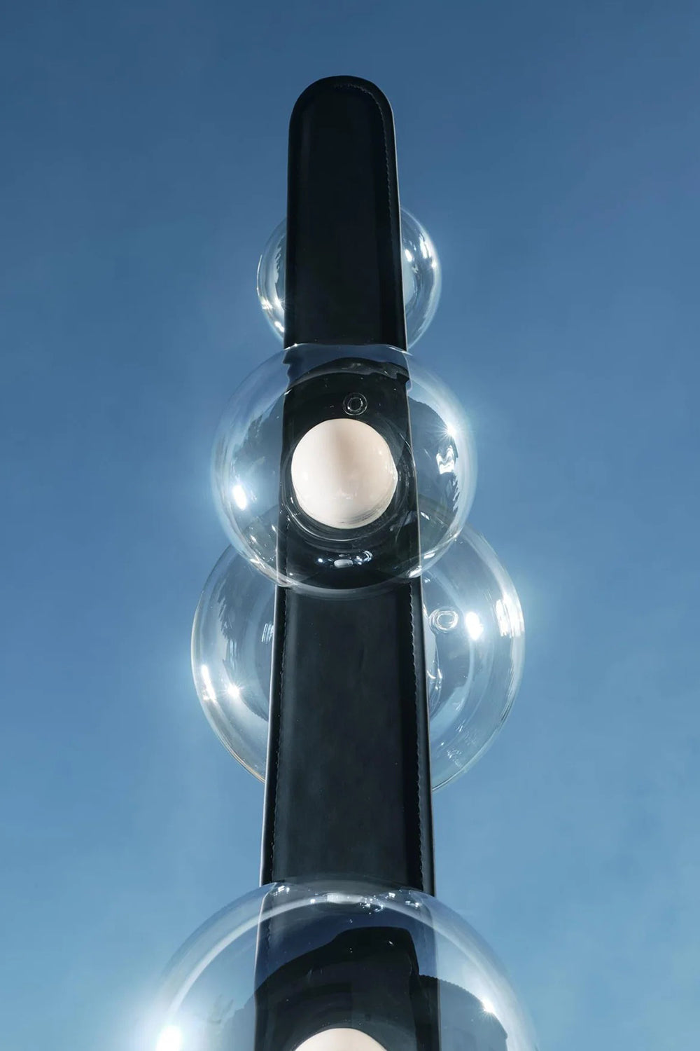 Drosia Dewdrop Floor Lamp | Glass, Metal | Low angle artistic shot looking up at the clear glass spheres on the black metallic pole against a bright blue sky background | Detail shot | vexa lamps