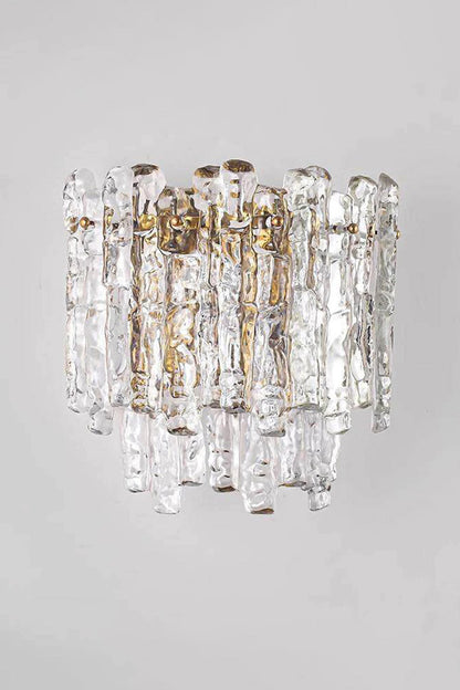 Elara Textured Cast Glass Wall Lamp | Textured Cast Glass, Polished Brass | Medium angle shot of the illuminated lamp against a neutral grey wall, demonstrating its shape and the dramatic textured glass effect in a corridor or entryway | vexa lamps