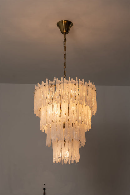 Ethereal Icicle Waterfall Chandelier | Glass, Metal | Full view of the fully illuminated tiered chandelier casting a dramatic warm light against a plain wall | vexa lamps